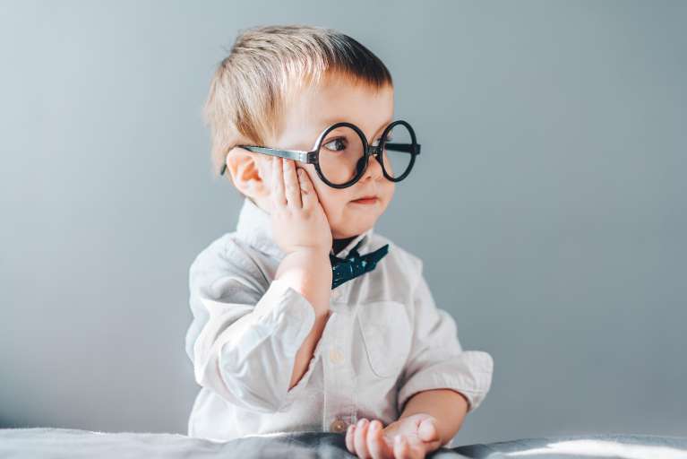 Smiling young boy in glasses and bow tie promoting kids' dental care.